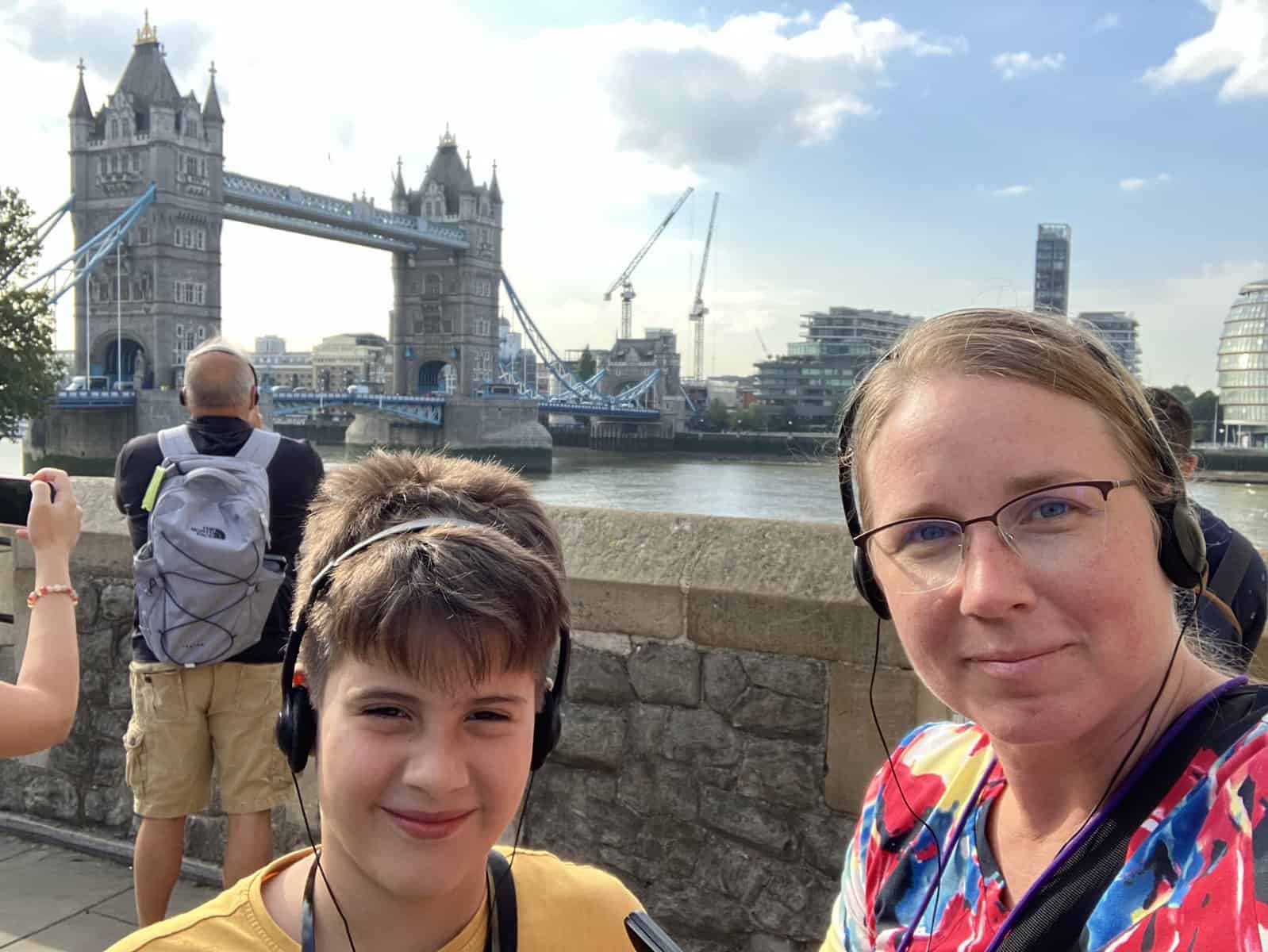 a boy and a woman in front of london bridge at the london tower wearing audio guides in london england